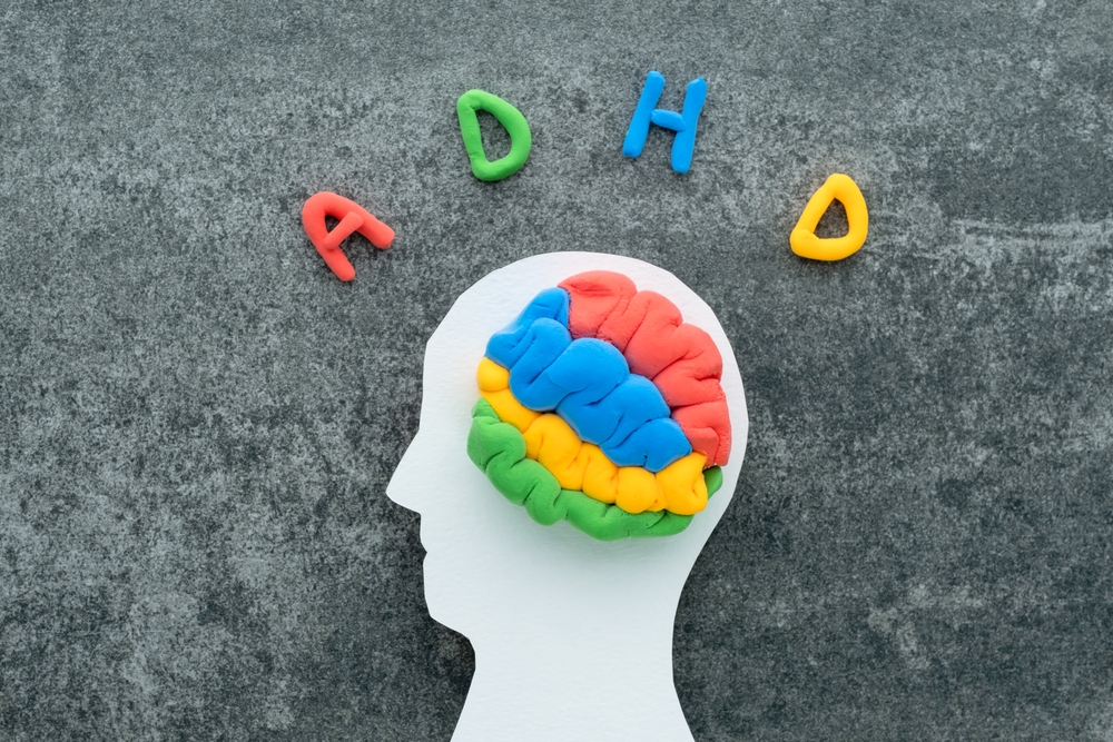 Colorful clay model of a brain inside a white silhouette of a head, with the letters “ADHD” arranged above it on a dark textured background.
