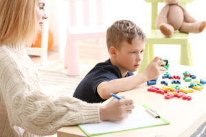 Young boy focused on colorful letter toys during a developmental assessment, while a woman observes and takes notes.