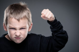 Young boy with an angry expression, raising his fist in a threatening gesture, symbolizing aggression or intense frustration.