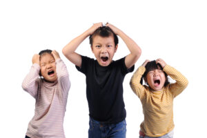 Three young children screaming and holding their heads in frustration or distress, expressing strong emotions against a white background.