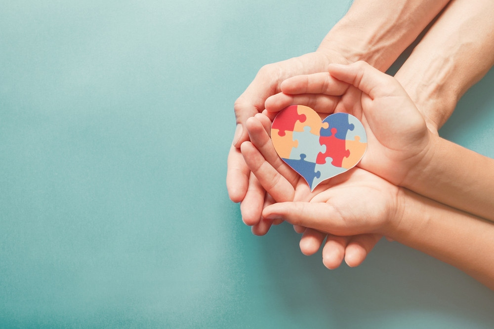Adult and child hands holding a heart-shaped puzzle piece symbol, representing autism awareness and support