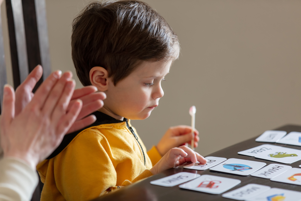 Young boy matching picture cards during at-home therapy as an adult applauds