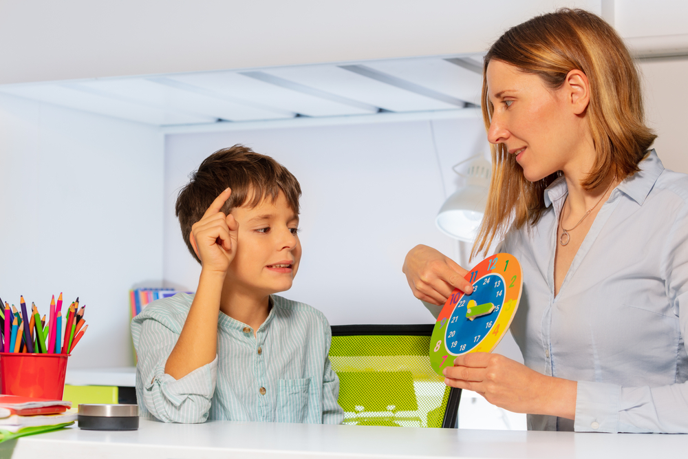 Woman teaching a young boy to tell time with a colorful learning clock