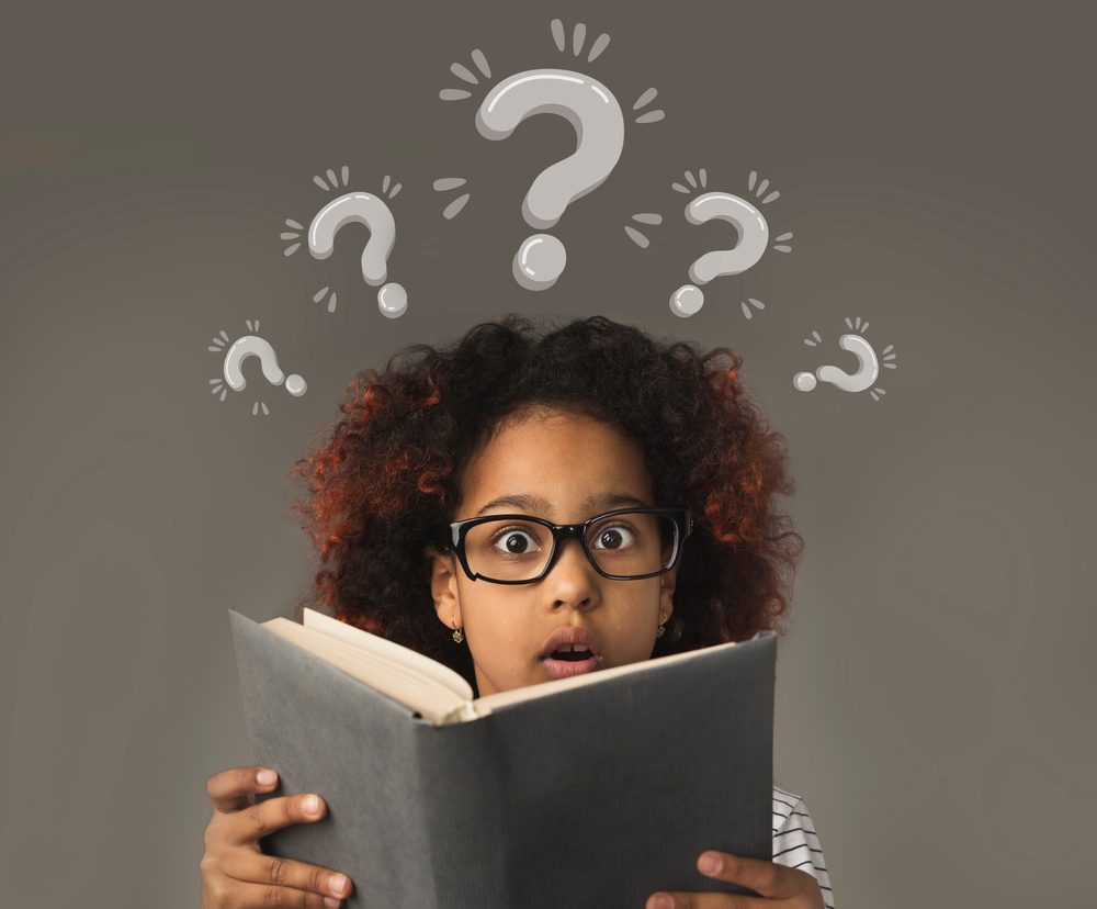 Surprised girl reading a book with question marks above her head.