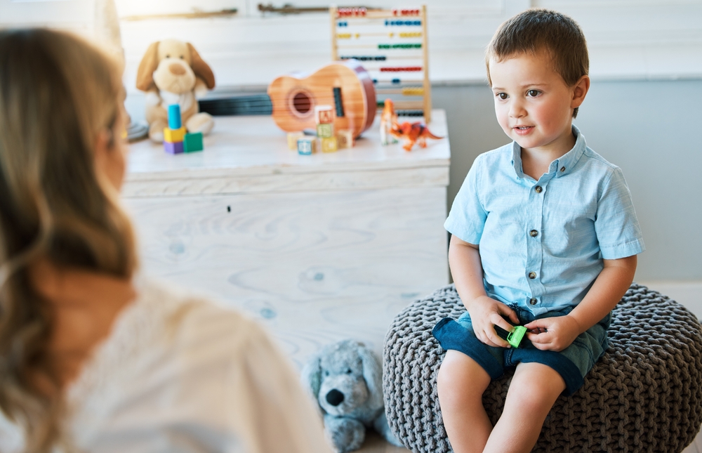 Young boy sitting on a pouff chair interacting with a female therapist who has her back to the camera.