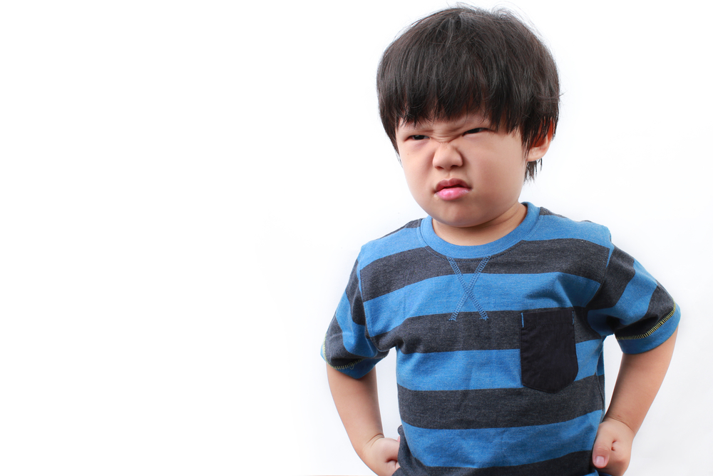 A young Asian boy wearing a black and blue striped shirt, grimacing and holding his fists tight.