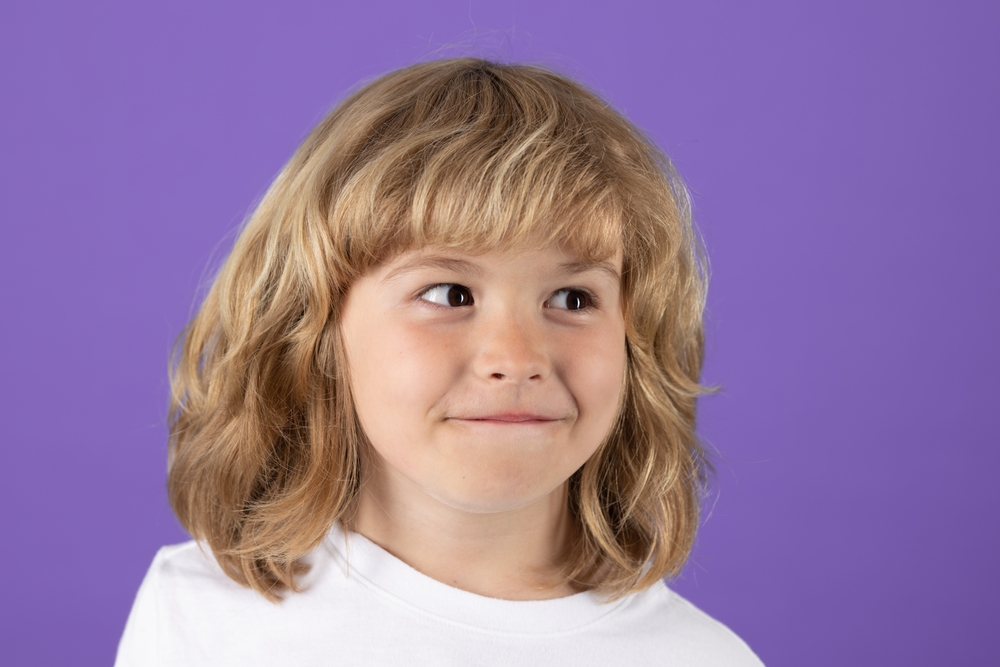 Brown-haired girl with bangs wearing a white t-shirt looking to her left.