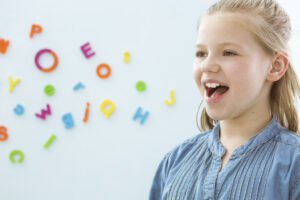 A young girl wearing a denim shirt, and her mouth is open. There are magnetic multicolored letters in the background.
