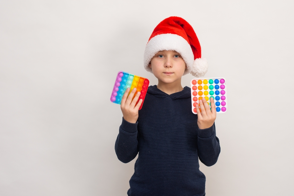 A young boy wearing a Santa hat holding identical fidget toys, one in each hand.