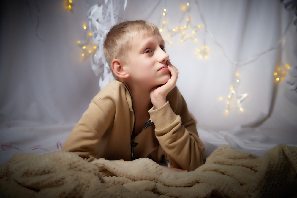 Blond-haired boy propped up on his elbows, admiring the star-shaped lights hanging around him.