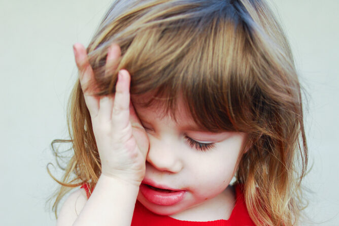 Brown-haired girl wearing a Christmas apron and rubbing her eyes from exhaustion.