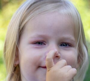 A young blond-haired girl touching her nose in a close-up photo