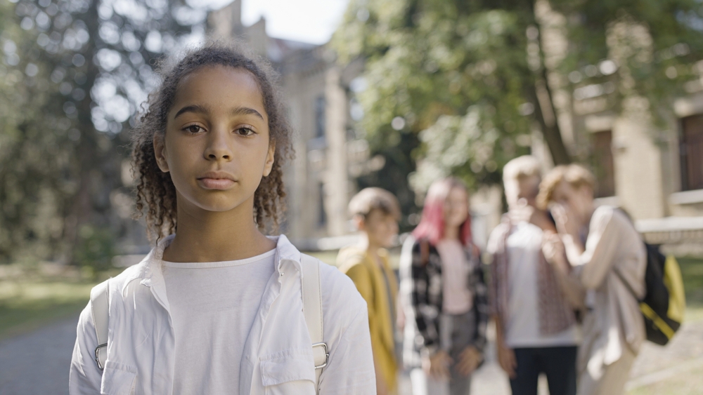 Young black girl giving a serious face to the camera while a group of kids behind her are laughing at a joke.