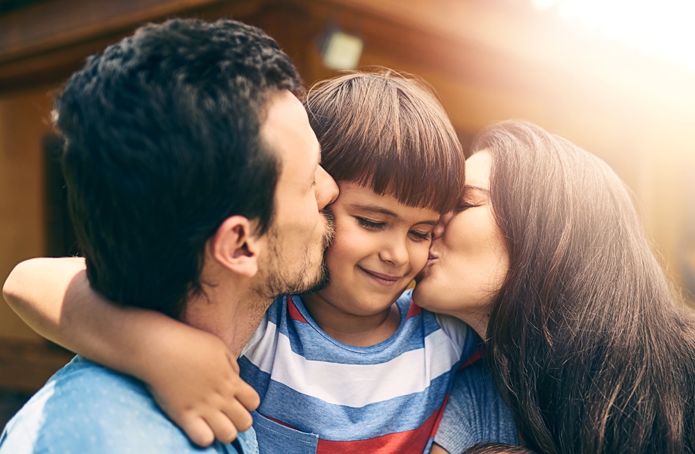 Young boy with brown hair, with his arms wrapped around his mom and dad.