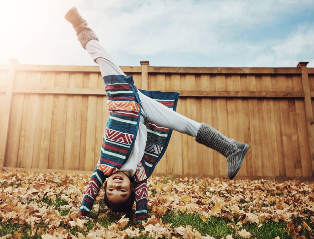 A young Asian girl performing a cartwheel in the leaves, wearing a sweater and woolly boots.