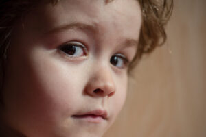 A close-up of a child with brown eyes and brown hair looking indifferent towards the camera.