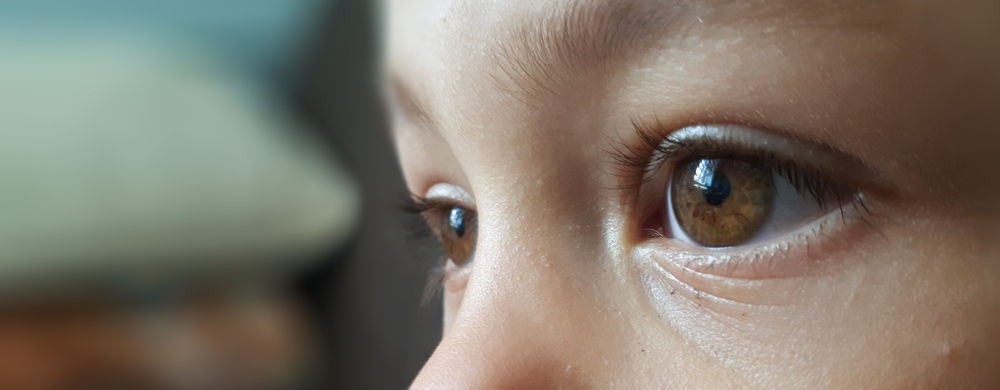 A side view close-up of a child’s brown eyes, bridge of their nose, and long eyelashes