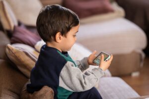 A young child with brown hair sitting on a sofa and using a cell phone to communicate.