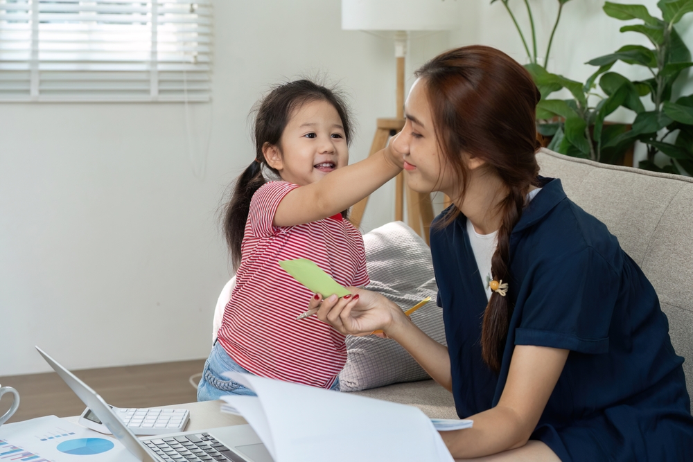 A young Asian girl in a red-striped t-shirt is working with her therapist at a coffee table at home. 