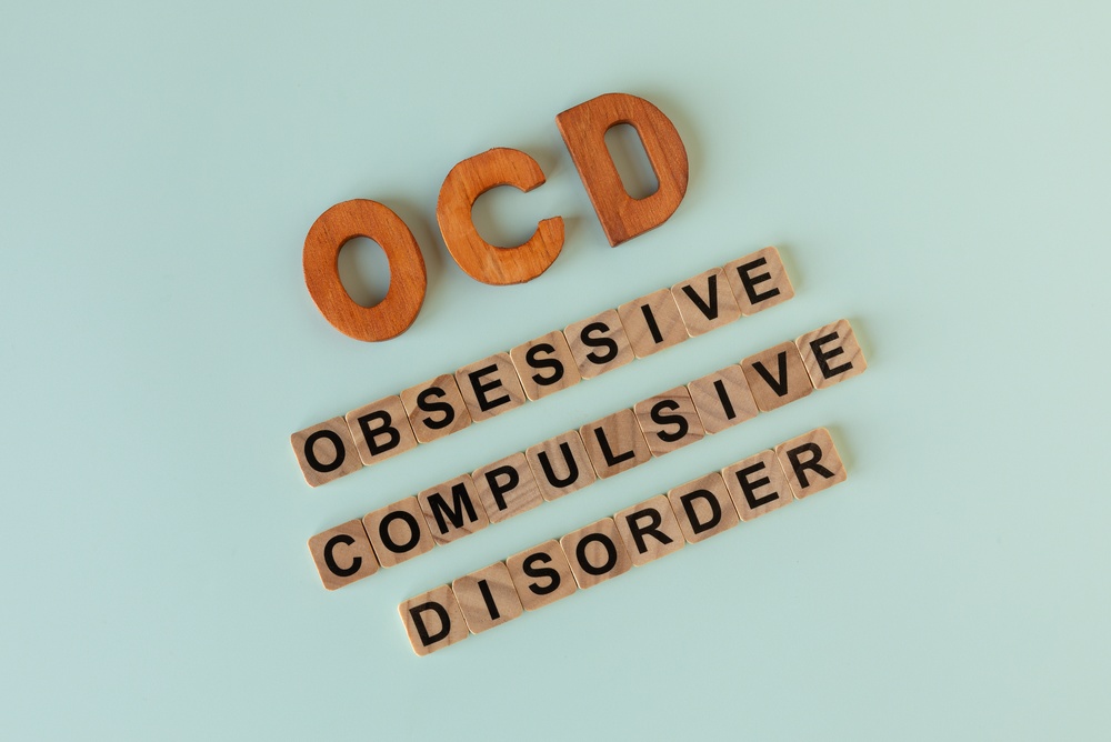 Wooden letter tiles and blocks spelling out "OCD" and "Obsessive Compulsive Disorder" arranged on a light blue background.