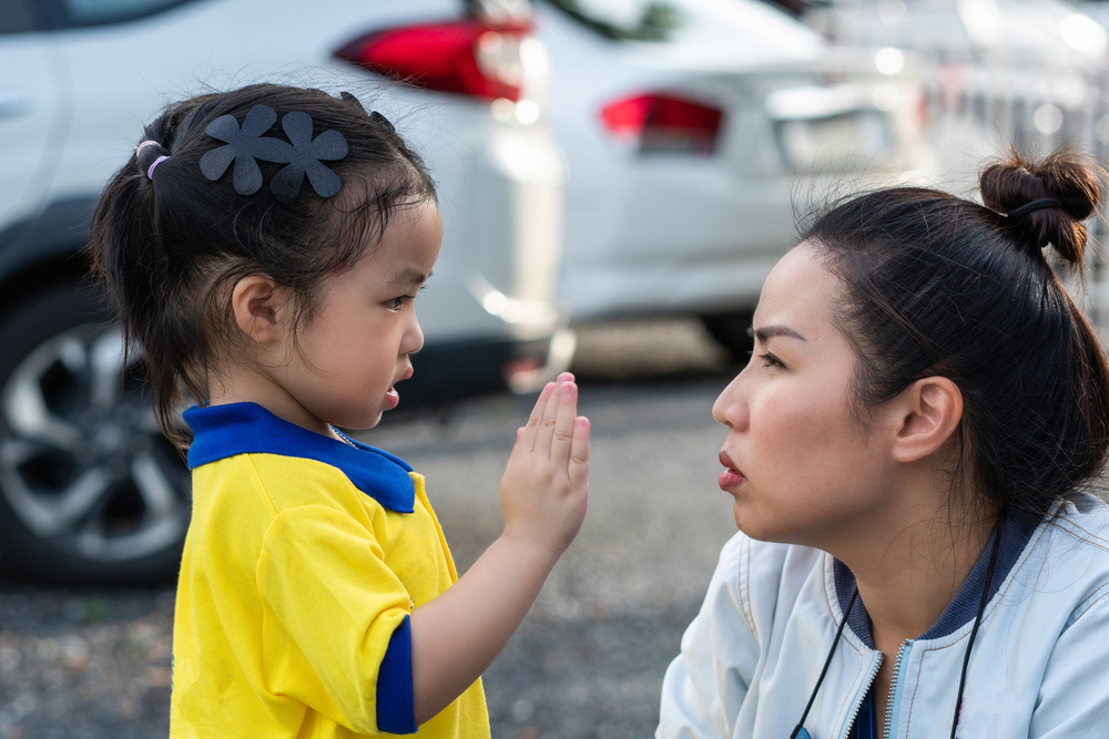 A young asian girl with black flower barrettes speaking to her mother using her hands