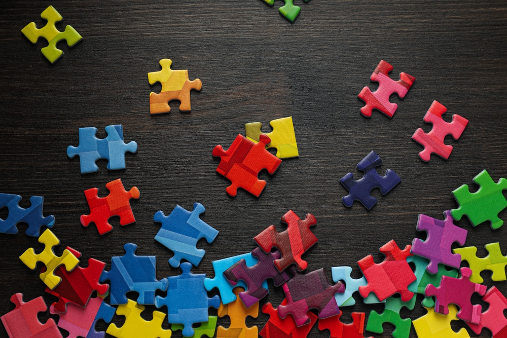  A table top with a multitude of puzzle pieces in different colors representing the autism spectrum.
