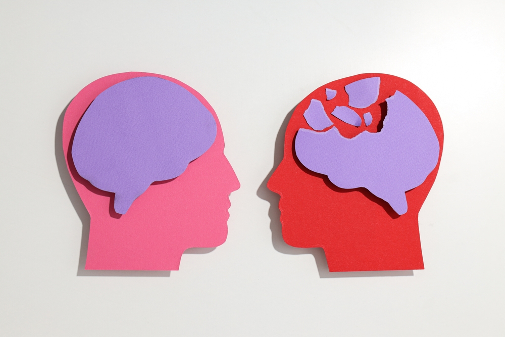 Paper cutout illustration of two head silhouettes, one with an intact brain and one with a fragmented, broken-apart brain 