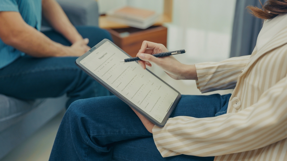 Behavior analyst taking notes on a tablet during a therapy session with a client