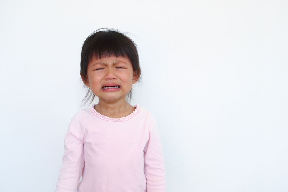 Small asian girl wearing a pink long-sleeve T-shirt with her eyes closed, crying and clenching her mouth.